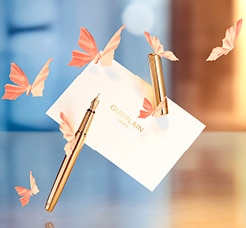 Guerlain arany toll és fehér kártya pillangókkal, elegáns háttérben.